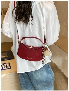 Detail of burgundy crescent shoulder bag with gold clasp and decorative plush bear charm