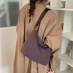 Detail view of brown checkered pattern fabric on a large crossbody bag worn with a coat