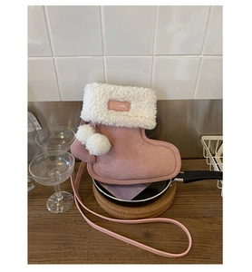 Detail van roze suède crossbodytas in de vorm van een laars met wit bont en pompons