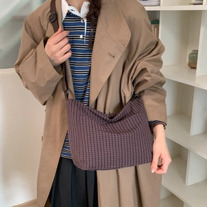 Detail of a large brown checkered canvas crossbody bag shown on a stylish trench coat
