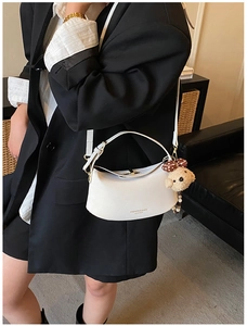 Side view of a white crescent shoulder bag with bear pendant in modern home setting