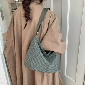 Detailed back view of a large green checkered canvas tote bag worn with a beige coat