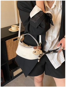 Chic white half-moon crossbody bag with cute teddy charm worn by a model in casual style