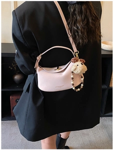 Pink crescent shoulder bag with plush lamb charm shown being worn on a black blazer