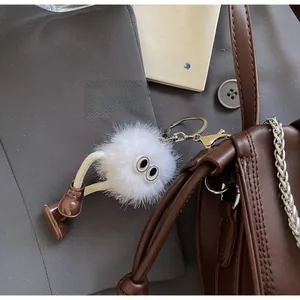 Close-up of white plush monster keychain charm with eyes and shoes on a leather handbag