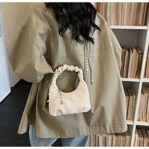 Detail of cream mini cloud bag with pleated handle, pearl bow, and metallic chain strap