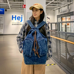 Detail of vintage denim backpack with brown drawstring and front zip pockets worn by model