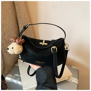 Close-up of black crossbody bag with gold buckle, logo print, and plush dog charm accessory