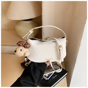 Detail of cream half-moon crossbody bag with golden twist lock and plush bear charm