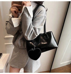 Detalle de bolso de hombro negro brillante con charm de corazón y textura de cuero elegante