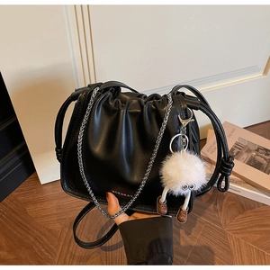 Detail of black pleated cloud bag with silver chain strap and white plush toy pendant