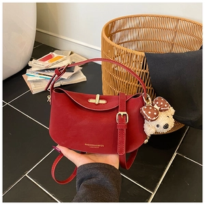 Detail shot of red leather half-moon shoulder bag with golden lock and plush bear charm