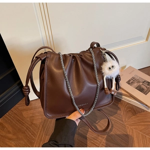 Close-up of brown faux leather pleated bag with gold logo and white plush charm detail