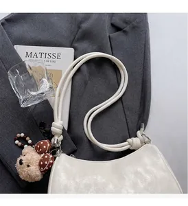 Close-up of cream leather dumpling bag featuring a knotted rope handle and a cute bear charm