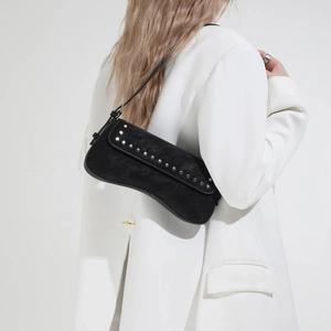 Close-up of minimalist black suede baguette bag with silver studs on a female model