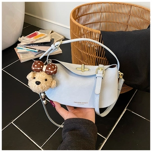 Detail of light blue leather handbag with golden twist lock and plush bear charm