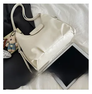 Detail view of cream soft leather hobo bag with teddy bear pendant on white bedding