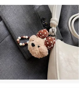 Detail of a beige teddy bear plush charm with a polka dot bow on a white leather bag
