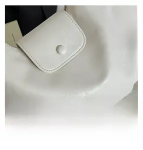 Close-up of white leather handbag flap showing fine texture and a magnetic button fastener