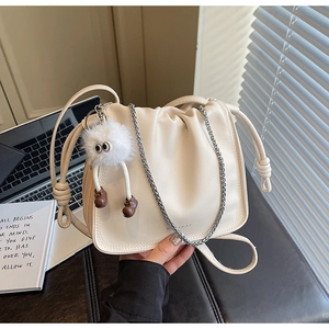 Detail of cream pleated crossbody bag featuring silver chain and cute plush monster charm