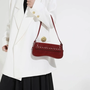 Detail of a deep red vintage baguette bag with silver studs and wavy bottom on a model