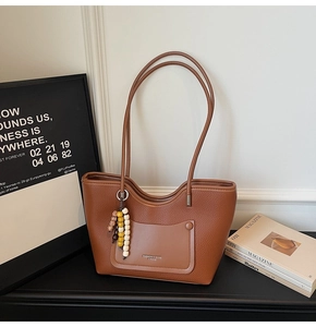 Detail of a brown leather tote with litchi grain texture and a beaded charm accessory