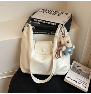 Detail of cream white leather hobo bag with a cute teddy bear charm on steps
