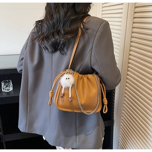 Detail view of a tan ruched crossbody bag with a metal chain and white plush charm pendant