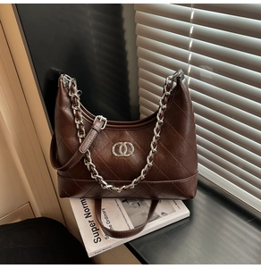 Detail van donkerbruine gewatteerde leren tas met zilveren ketting en metalen gesp