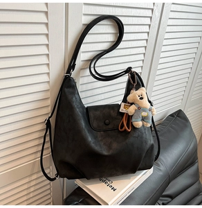 Detail of black matte Hobo bag with cute teddy bear charm on white shutter background