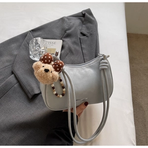 Detail of grey crescent shoulder bag with a plush bear charm and sleek branding text