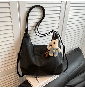 Detail of a vintage black hobo bag with a cute bear charm on a white book and leather sofa