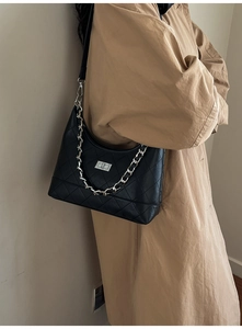 Detail van zwarte gewatteerde hobo tas met zilveren ketting en sluiting op beige jas