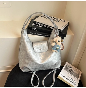 Silver metallic hobo bag on chair featuring a cute teddy bear charm and snap closure