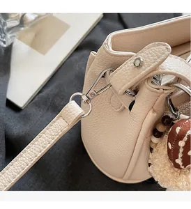 Close-up of beige lychee grain leather handbag with silver metallic rotating buckle and charm
