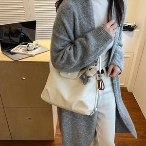 Close-up of white synthetic leather texture and cute plush bear accessory on the bag