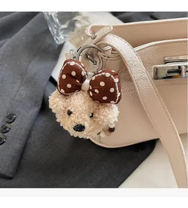 Detail of a plush bear charm with a polka dot bow attached to a stylish handbag