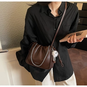 Detail of dark brown ruched crossbody bag featuring silver chain and cute monster charm