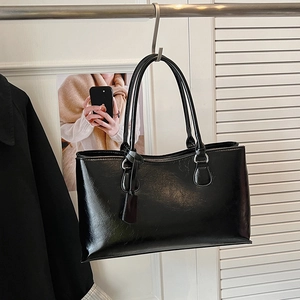 Detailed view of black glossy PU leather tote bag with slim shoulder straps and metal rings