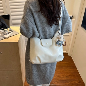 Detail of a large cream leather tote bag with a cute bear plush keychain on a model