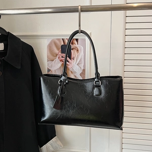 Detail view of glossy black tote bag with wrinkled texture hanging in home setting