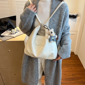 Detail view of white pleated leather tote bag with cute teddy bear plush charm and flap closure