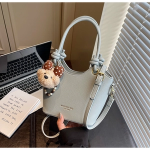 Close-up of light blue bucket bag with lychee grain leather and bear pendant accessory