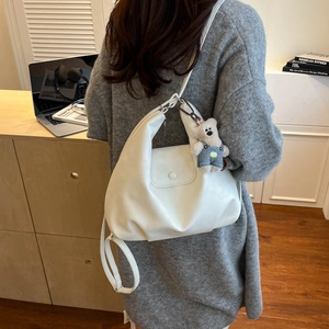 Detailed side view of white hobo bag with cute blue bear charm worn by a person