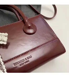 Close-up of wine red faux leather bag with elegant lace trim and brand logo engraving