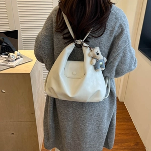 Detail view of cream white leather backpack with a cute blue bear plush charm