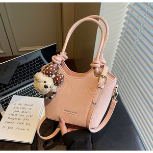 Detail of light pink pebble leather bucket bag with unique knotted handles and bear charm