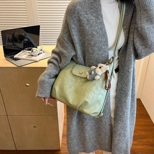 Detail view of a pale green leather tote bag featuring a cute teddy bear plush charm