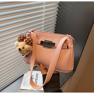 Detail of pink lychee leather handbag featuring a metal turn-lock and plush bear charm