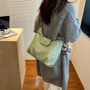 Detail of light green crescent shoulder bag with cute white bear plush charm on grey sweater